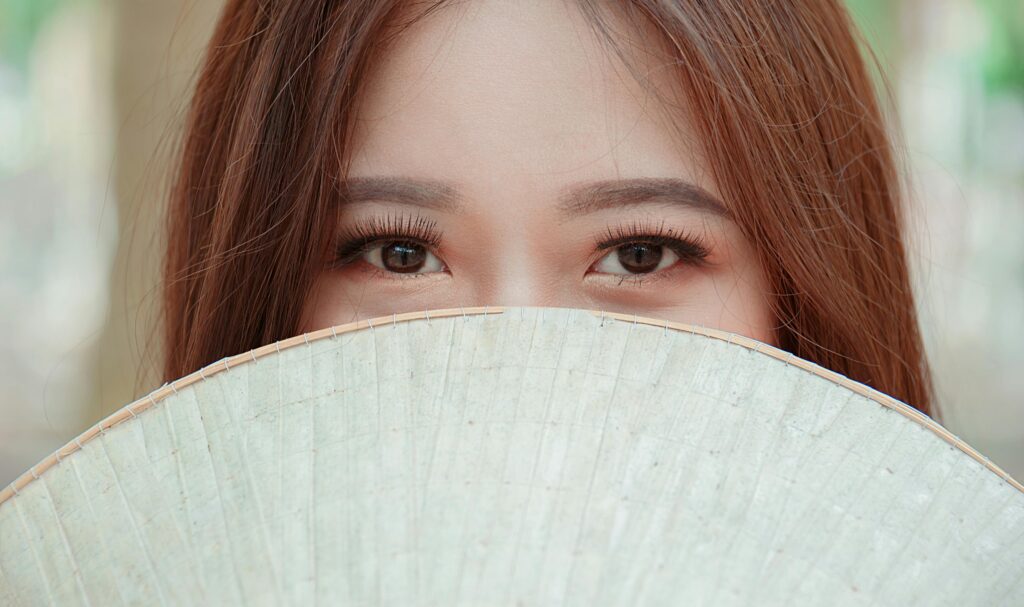 Elegant portrait of a woman partially hidden by a traditional Asian fan.