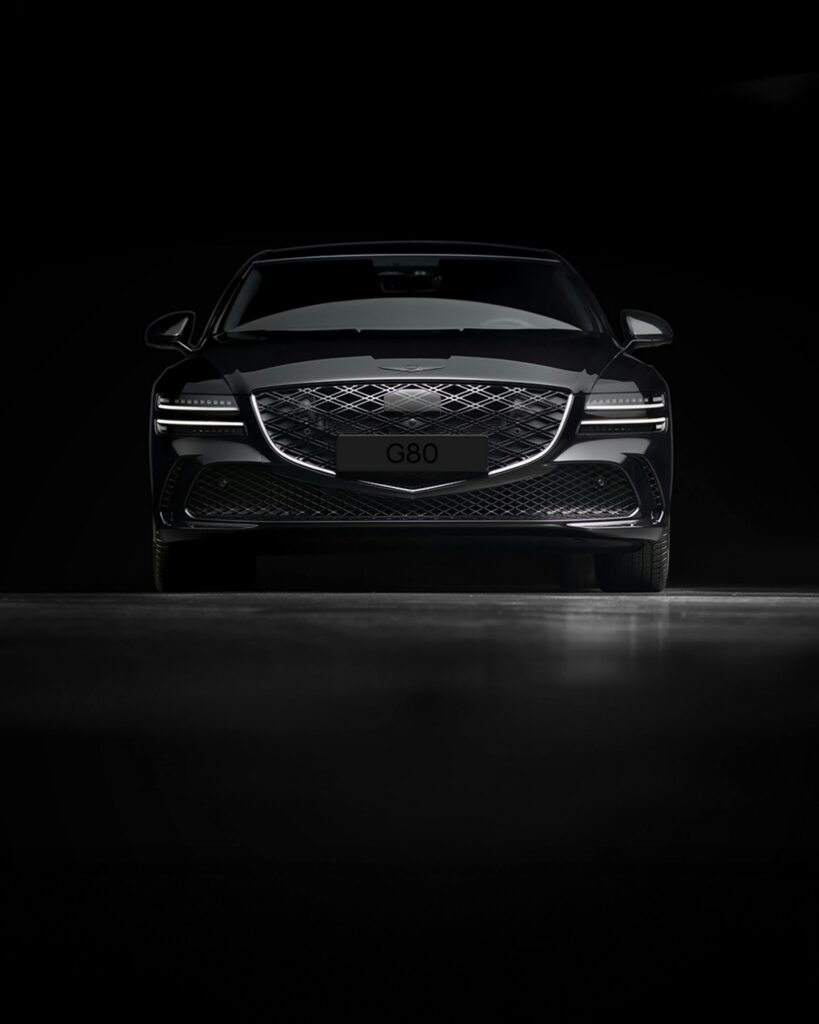 A luxury Genesis G80 sedan showcased in a dark studio. Front view highlights design.