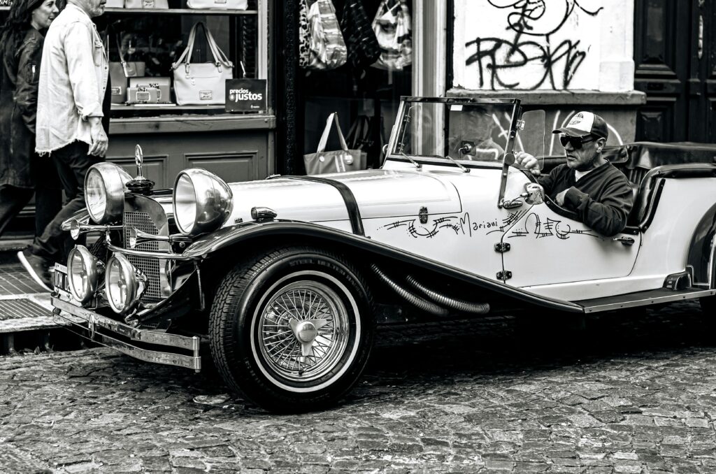Black and white photo of a driver in a vintage car on a cobblestone street in Buenos Aires, Argentina.